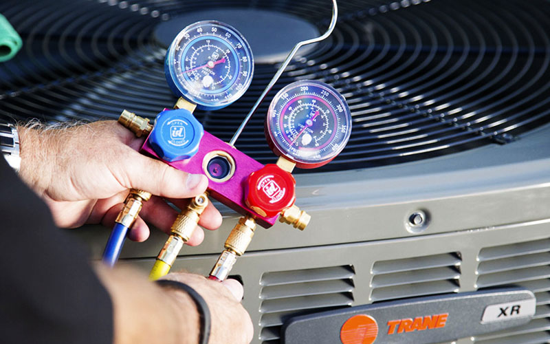 Male HVAC technician's hands holding a pressure gage over a Trane HVAC system.